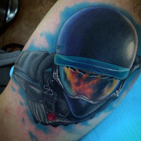 Realistic color tattoo of a skydiver in a helmet and goggles, reflecting fiery colors, with a blue sky background on the bicep