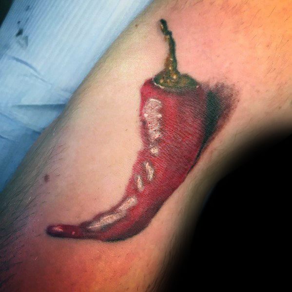 Hyper-realistic red chili pepper tattoo with detailed shading and highlights, creating a glossy, three-dimensional effect on the skin.