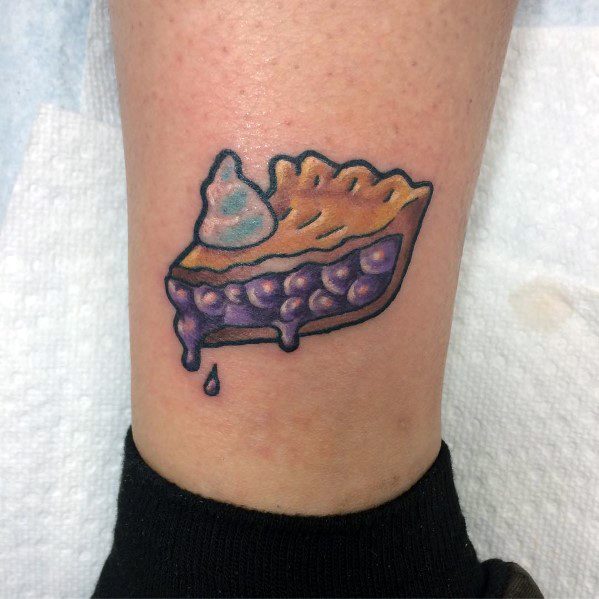 Colorful blueberry pie tattoo with dripping filling and a dollop of whipped cream, featuring a playful and cartoon-style design
