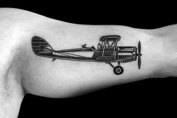 Black and grey dotwork tattoo of a vintage biplane on the inner arm, featuring intricate shading and fine line details for a classic aviation look.