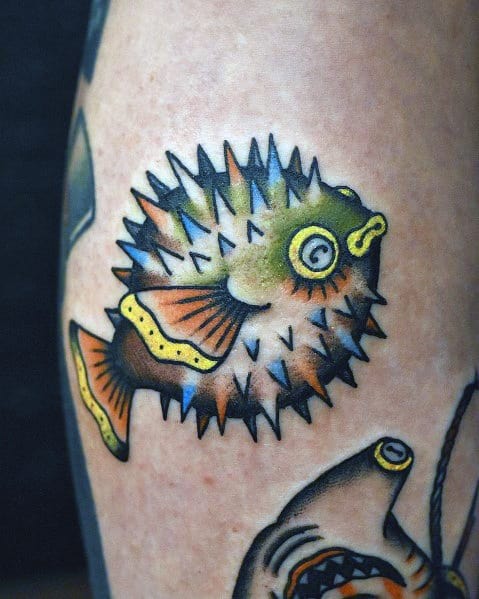 Traditional pufferfish tattoo with bold black outlines, vibrant green and orange hues, and sharp spikes, creating a classic and dynamic look.