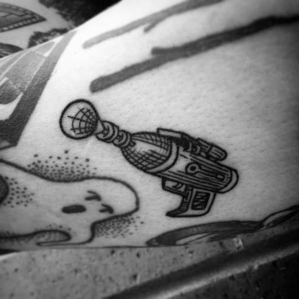 Small black and grey ray gun tattoo with fine line details, a vintage sci-fi aesthetic, and subtle shading for a classic retro-futuristic look.
