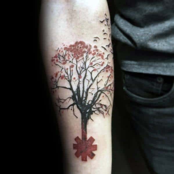 Forearm tattoo featuring a tree growing from the Red Hot Chili Peppers logo, with birds flying from the branches for a creative design.