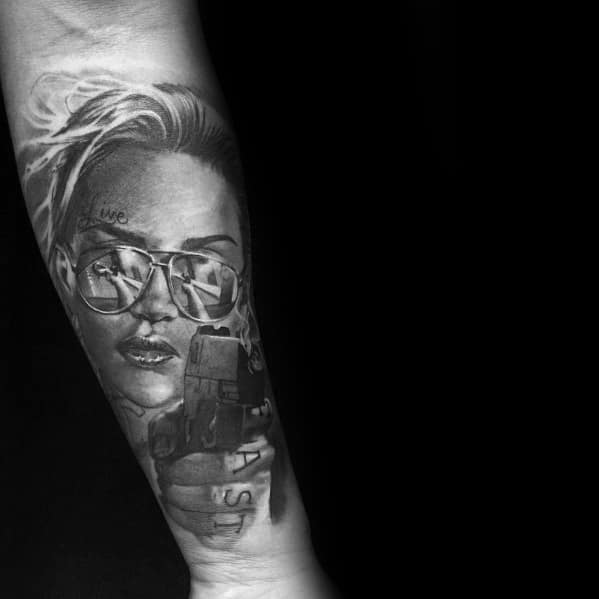 Tattoo of a woman wearing sunglasses reflecting a gun, blending realism and dramatic shading for a bold and intense design.
