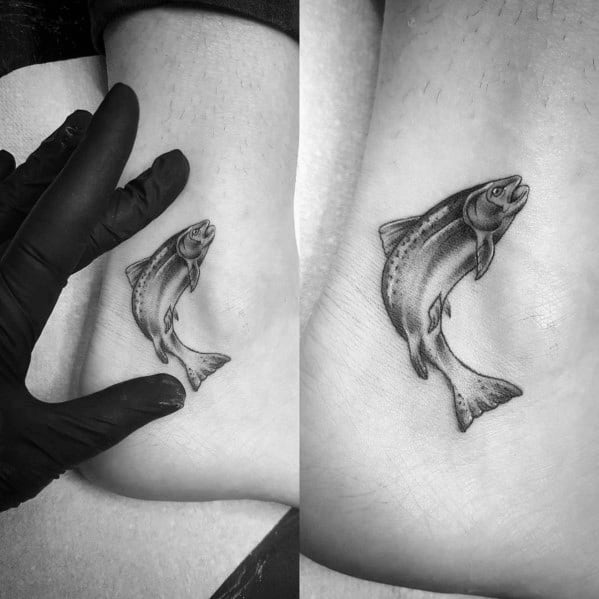 Small black and grey tattoo of a leaping salmon with fine shading and smooth details, placed on the ankle for a subtle yet elegant design.