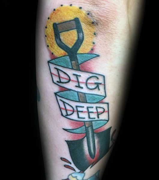 Shovel tattoo with a ribbon wrapped around it reading "Dig Deep," set against a sun backdrop, symbolizing determination and inner strength.