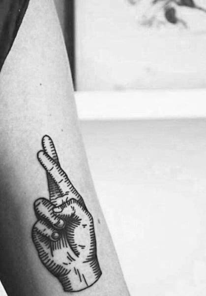 black ink tattoo of a hand with crossed fingers, designed with bold lines and shading for a vintage, illustrative style on the forearm