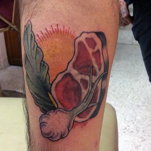 Tattoo of a raw steak with garlic, a leafy herb, and a radiant sun in the background, creating a bold and rustic food-inspired design