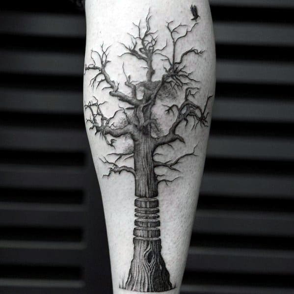 Black ink tree tattoo on the leg, featuring a detailed trunk wrapped in rings, twisted branches, and a small bird for a symbolic and artistic design.