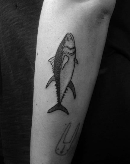 Minimalist black and grey tuna fish tattoo on a man's forearm, featuring fine linework and subtle shading for a simple yet detailed design.