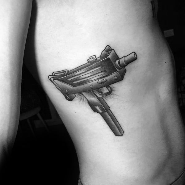 Realistic black and grey Uzi tattoo on the ribcage with fine shading and depth, creating a bold and detailed firearm design.