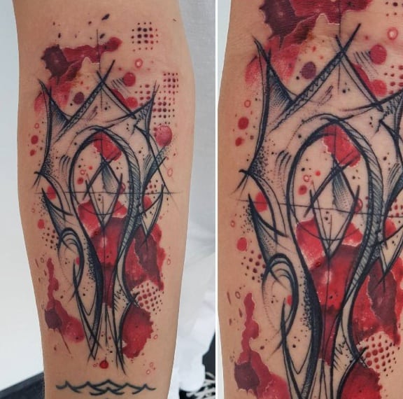 Abstract sketch-style tattoo of the Horde emblem from World of Warcraft, featuring bold black lines, red splashes, and geometric details, inked on the forearm.