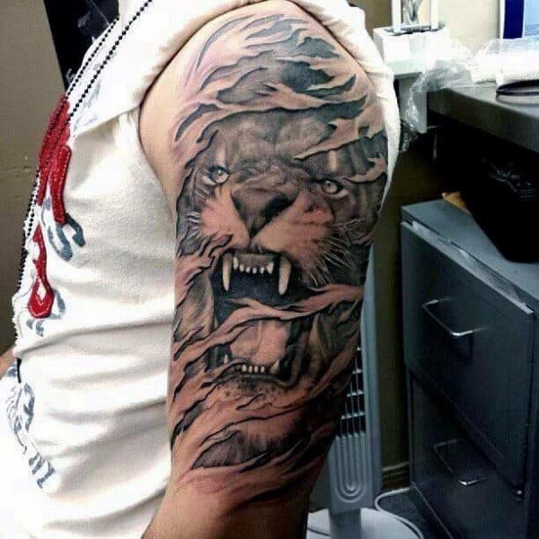 Tattoo of a roaring lion on a person's upper arm with swirling details