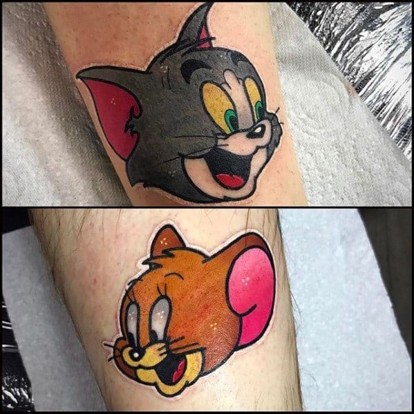 Matching tattoos of Tom and Jerry's smiling faces in vibrant colors, inked on separate arms in bold cartoon style.
