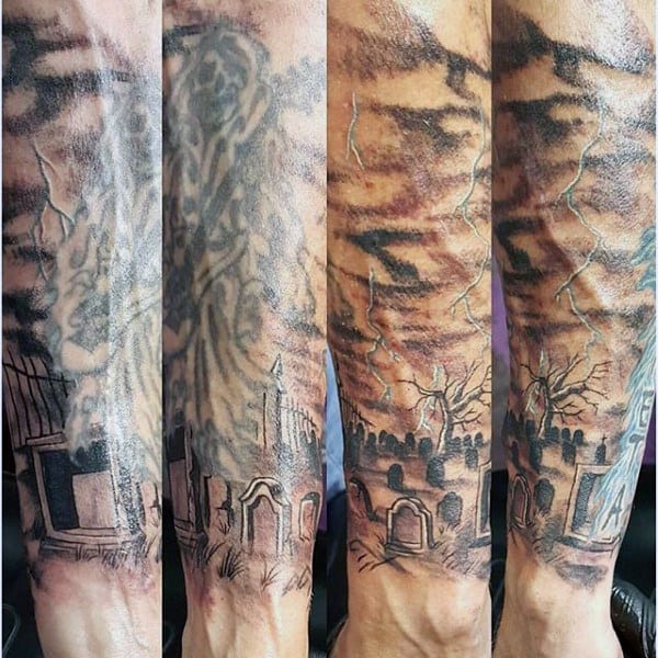 Forearm tattoo depicting a graveyard scene with gravestones, trees, and cloudy skies