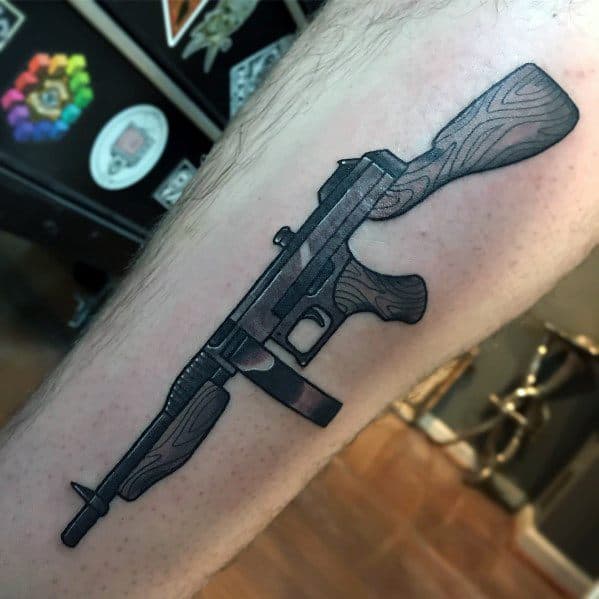 Bold Tommy gun tattoo with clean black outlines, wood grain details, and precise shading, creating a sharp and classic firearm design on the leg.