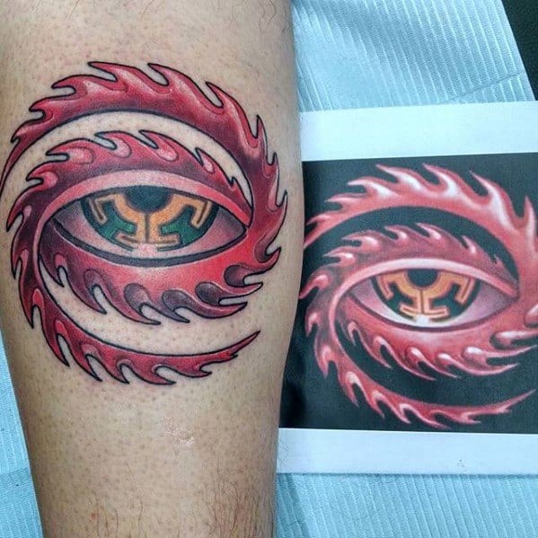 Colorful Tool-inspired tattoo of a red flaming eye with a green and gold iris design, matching the reference image placed beside it.