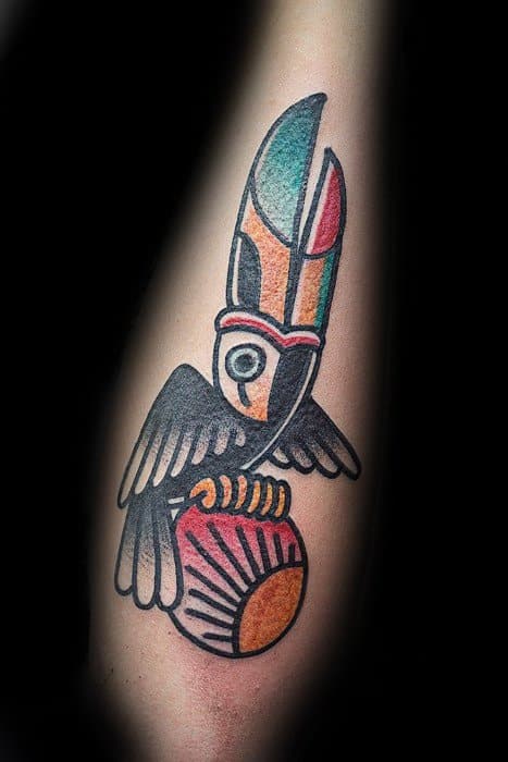 Abstract toucan tattoo with bold outlines and tribal-inspired patterns, featuring geometric shapes and muted colors on the forearm.