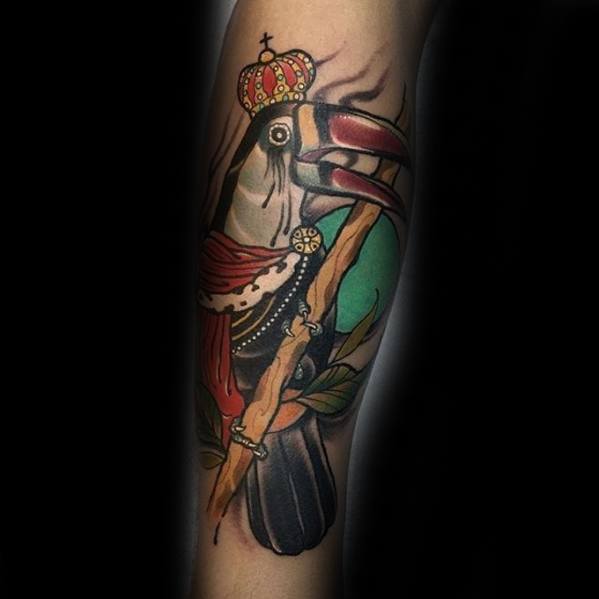 Regal toucan tattoo dressed as a king with a crown and red robe, perched on a branch with rich colors and bold traditional lines.