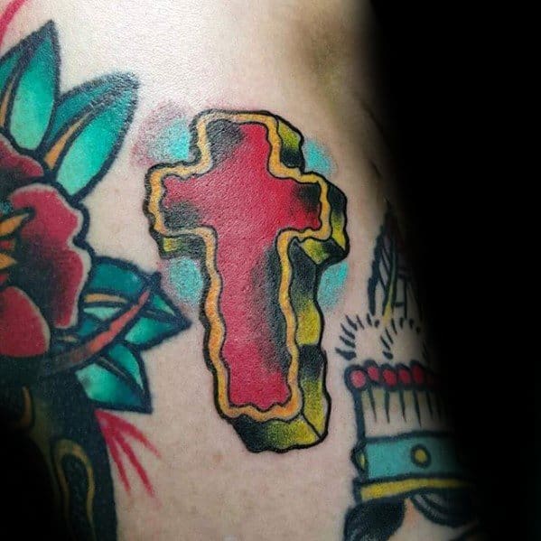 Bold traditional cross tattoo with red center, yellow outline, and blue highlights, surrounded by classic old-school elements.