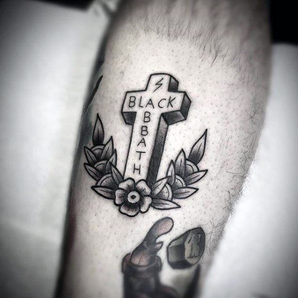 Black and grey tattoo of a cross reading "Black Sabbath" with a lightning bolt at the top, surrounded by leaves and a flower at the base.