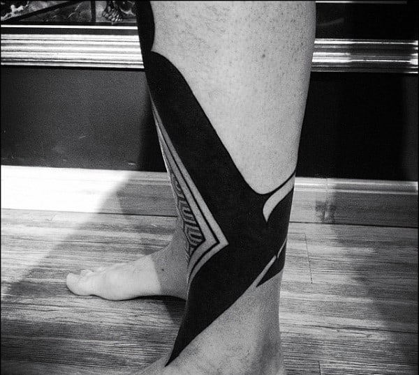 Black geometric tattoo on a person's leg, extending from ankle to below the knee