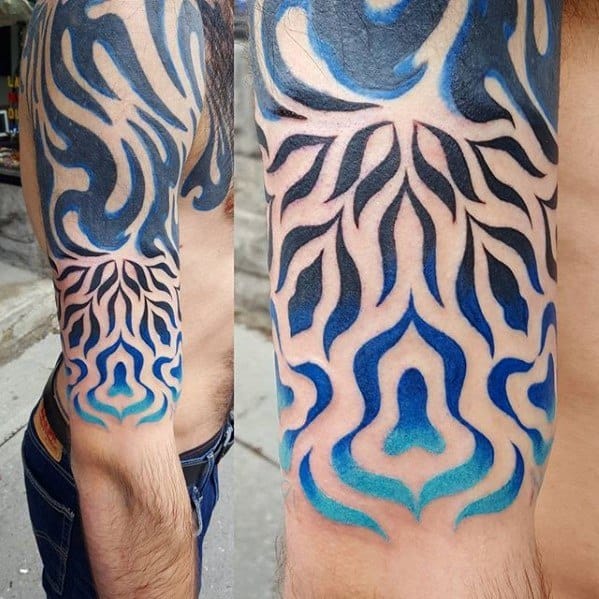 Bold tribal-style tattoo with blue and black flame-like patterns flowing down the arm in a symmetrical design.