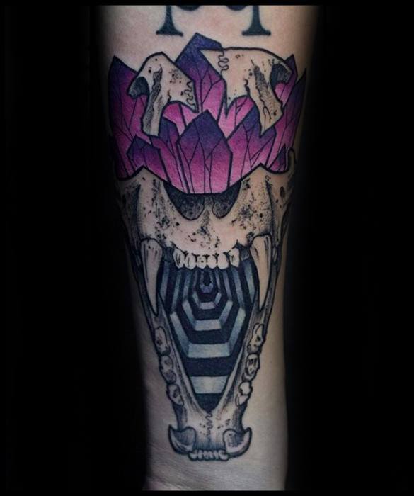 Tattoo of a roaring animal skull with a black-and-white hypnotic spiral inside its mouth and purple crystals emerging from the top.
