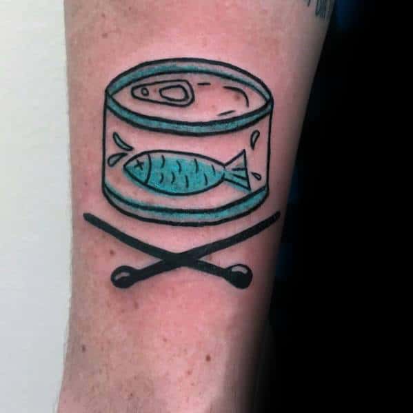 Minimalist tuna can tattoo on a man's forearm, featuring bold black outlines, simple shading, and crossed chopsticks for a playful design.