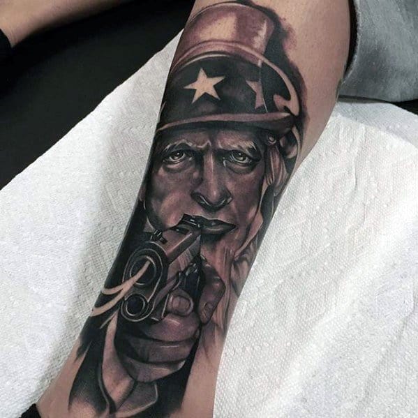 Realistic Uncle Sam tattoo in dark tones, staring intensely while pointing a gun forward with striking depth and smooth shading.