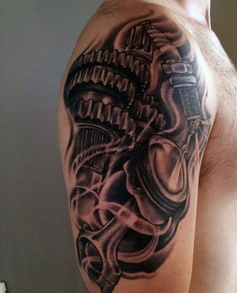 A detailed black and grey tattoo of mechanical gears covering a man's upper arm and shoulder