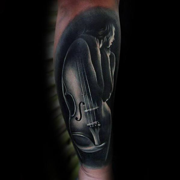 Elegant black and gray tattoo of a nude woman whose body forms the shape of a violin, blending human form with musical symbolism on the forearm.