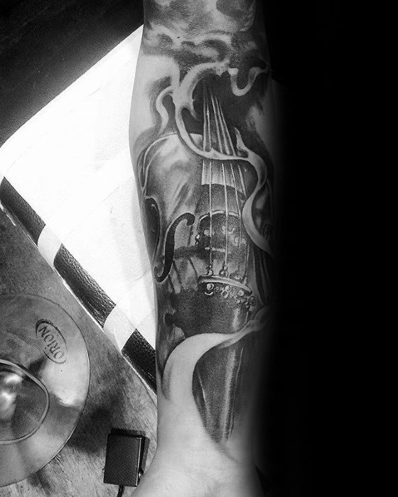 Black and gray forearm tattoo of a violin with swirling smoke-like accents, blending realism and abstract elements in a dramatic composition.