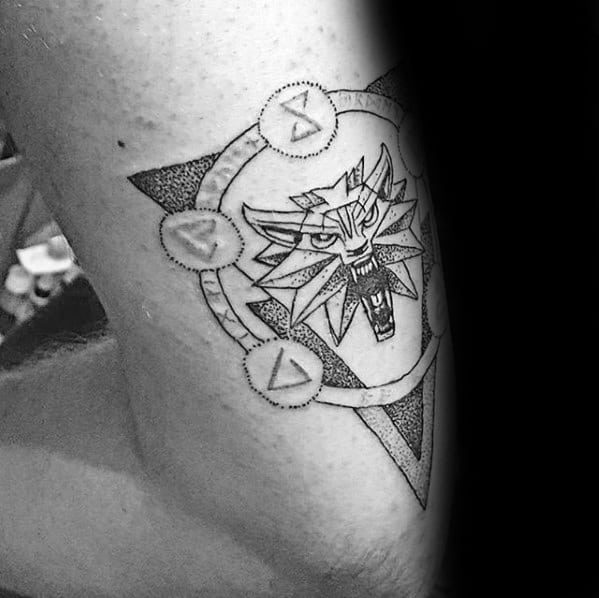 Dotwork Witcher tattoo on the upper arm featuring the wolf medallion inside a triangle with magical sign symbols in a circular pattern.