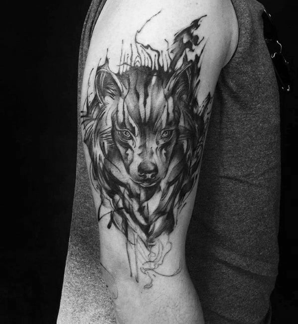 Black and grey wolf tattoo on upper arm with intense stare, abstract brushstroke textures, and flowing sketch-style linework.