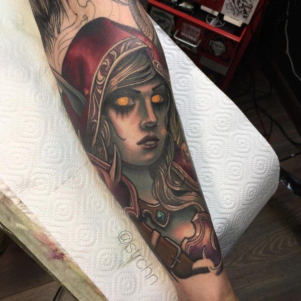 Detailed tattoo of a female World of Warcraft character with glowing eyes, wearing a red hood and armor, inked on a forearm.