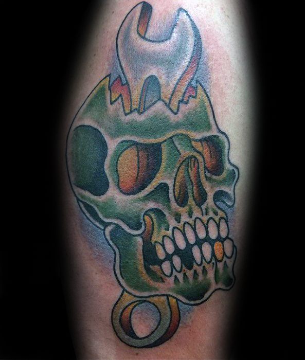 Colorful tattoo of a green skull with a wrench embedded in the top, combining mechanical and anatomical elements in a surreal style.