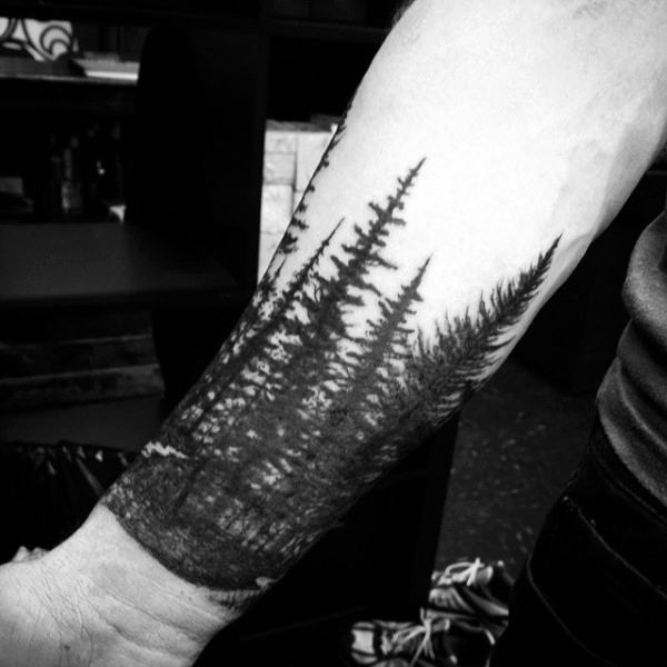 Black and white tattoo of a forest scene on a forearm