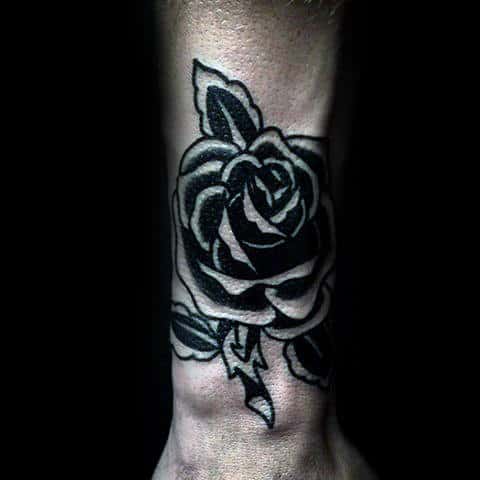 Black and white rose tattoo on a person's wrist with leaves and thorns