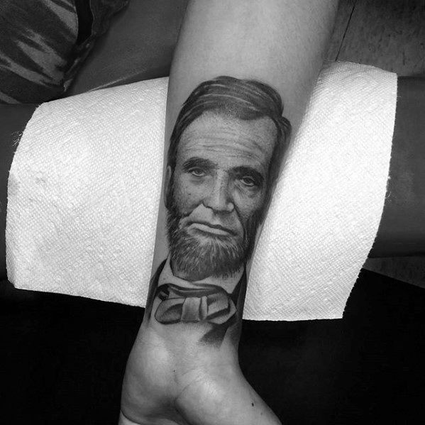 Black and white tattoo of Abraham Lincoln in a bow tie on a person's arm