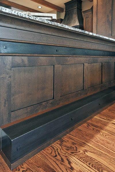 Rustic wood bar with black metal foot rail and granite countertop on polished hardwood flooring.