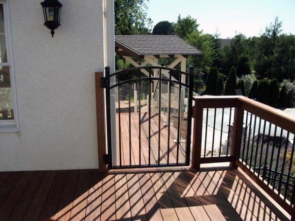 A wooden deck with a sleek black gate, overlooking a garden and pergola