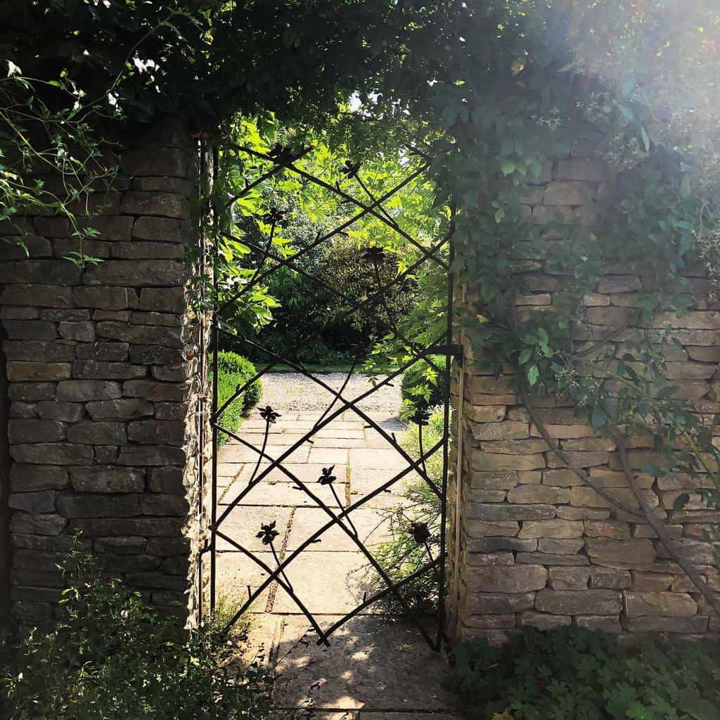 thin metal garden gate stone wall paved path