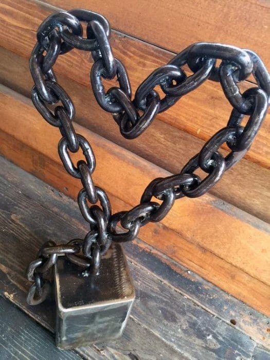 A heart-shaped chain connected to a metal block, set against a wooden background