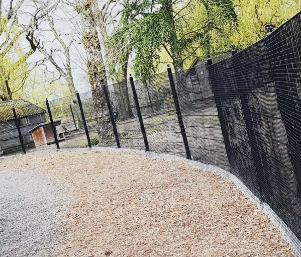 Curved black fence stands against a backdrop of trees and wood chips