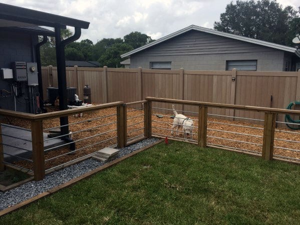Fenced backyard with a white dog on a leash, surrounded by grass and a sturdy wooden fence
