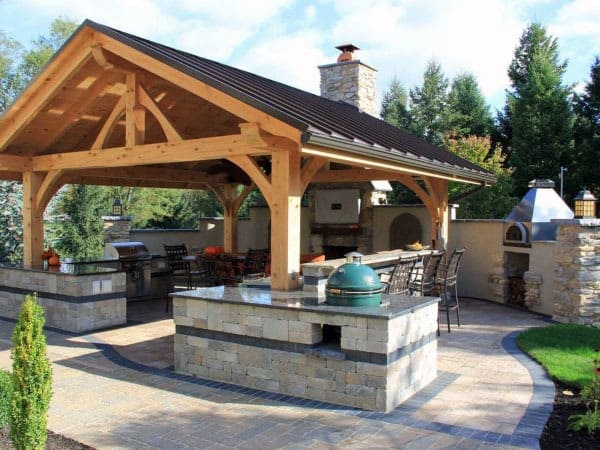 Spacious pavilion with a wooden frame, outdoor kitchen, pizza oven, and large seating area for dining.