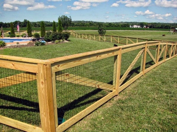 Wooden fence surrounds a grassy field beneath a blue sky dotted with fluffy clouds