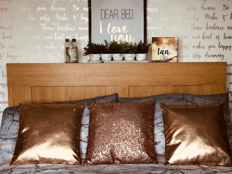 Wood headboard with copper-colored pillows and decorative wall art.