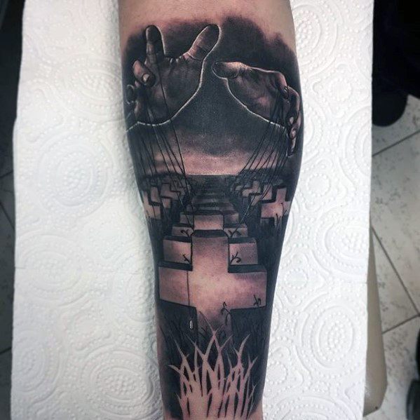 Forearm tattoo of hands controlling strings over military graves, inspired by Metallica’s Master of Puppets album cover art.